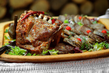 Assorted meat on a wooden tray cooked on fire, ribs and steaks with salad and hot pepper, a restaurant dish, a background of logs, a lot of meat for a big company