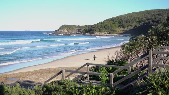 An ocean bay beach with a serfer walking towards the shore.