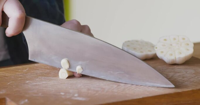 Woman chopping garlic clove on cutting board