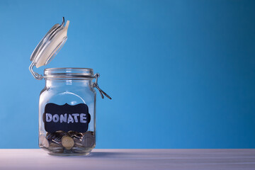 Glass jar with coins with chalk tag Donate on a blue background. Donation and charity concept. Copy space.