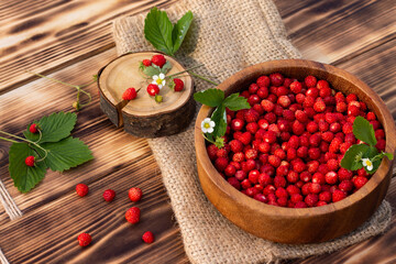 A wooden bowl of red ripe wild strawberries and flowers on old wooden surface.