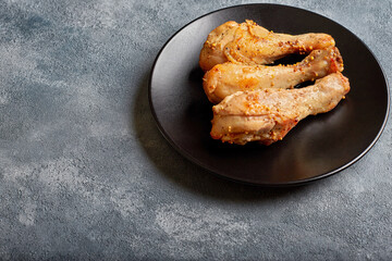 Three baked chicken drumsticks on a black plate