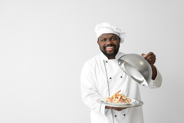 Male African-American chef with tasty dish on white background