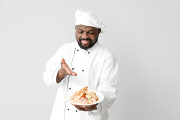 Male African-American chef with tasty dish on white background