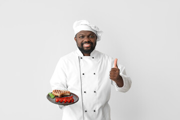 Male African-American chef with tasty dish on white background