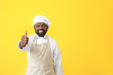 Male African-American chef showing thumb-up on color background