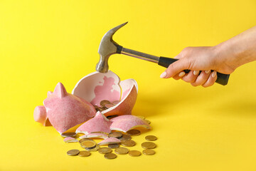 Hand with hammer and broken piggy bank on color background