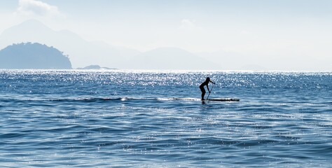 Obraz premium Silhouette of a woman stand up paddle surfing at the sea in Brazil