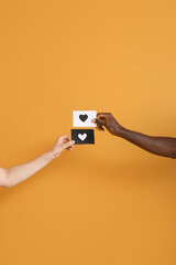 Hands of Caucasian woman and African-American man holding paper sheets with drawn heart on color...