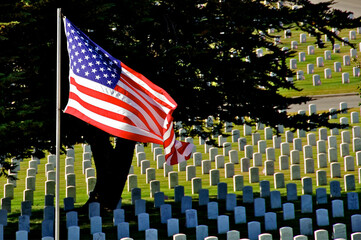 American Flag flies over headstones of military veterans and family. Golden Gate National Cemetery,...