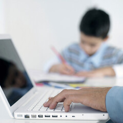 Boy doing homework while his father using laptop