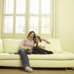 Obraz premium Mother and daughter sitting on the couch holding green apples