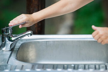 Baby try to turn off water faucet but water still leak. A child's hand turning off the tap. Save...