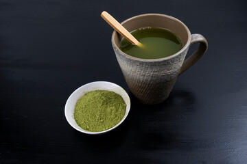 matcha tea brewed in a brown bowl and matcha powder on the side