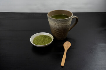 matcha tea brewed in a brown bowl and matcha powder on the side