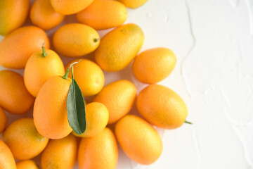 Fresh kumquats, small exotic citrus fruits, on a white textured background