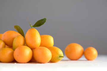 Kumquats, small citrus fruits, on a white textured surface, gray background