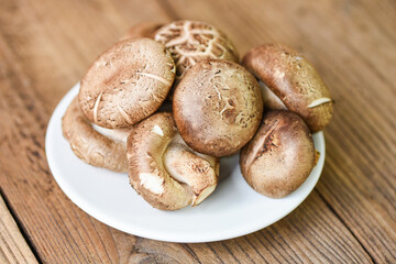 Fresh mushrooms on white plate and wooden table background - Shiitake mushrooms