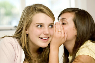 Girl whispering into another girl's ear