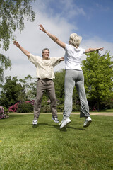 Senior man and woman jumping with their arms outstretched