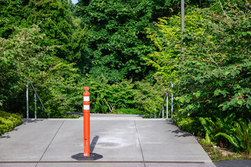 Orange caution pilon in the middle of a concrete walkway in a park setting
