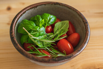 Tomatoes, rosemary and basil in a bowl. Fresh vegetables and herbs close up on wooden background