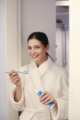 Woman in bathrobe holding toothpaste and toothbrush