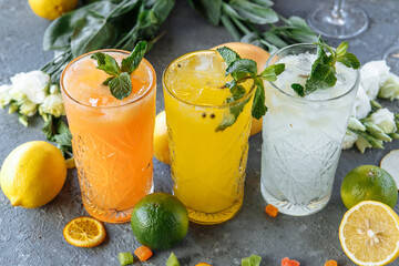 Summer fresh cold drink beverages. Ice Lemonade in the jug and lemons and orange with mint on the table outdoor. Orange lemonade in a glass - obrazy, fototapety, plakaty