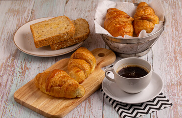 freshly baked croissants and whole wheat bread with black coffee on wooden table for breakfast