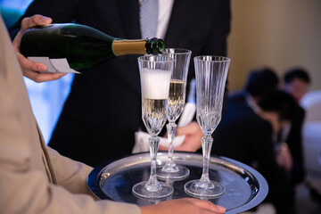 Hotel bar manager pouring white wine in glasses'