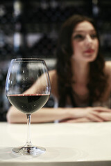 A glass of red wine with woman in the background