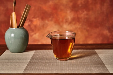 A cup of black tea against a vintage orange backdrop with tea tools and a tea canister.