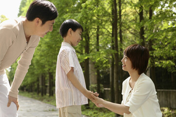 Boy and woman holding hands while looking at each other, man watching