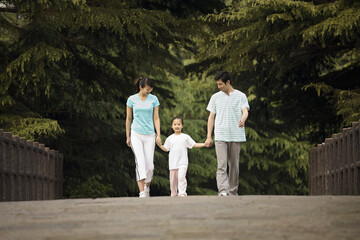 Fototapeta premium Girl holding hands with parents while walking in the park