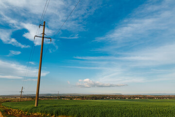 Fototapeta na wymiar A row of poles of a power line in a field near a dirt road under a clear sky. Electricity transmission line, power supply