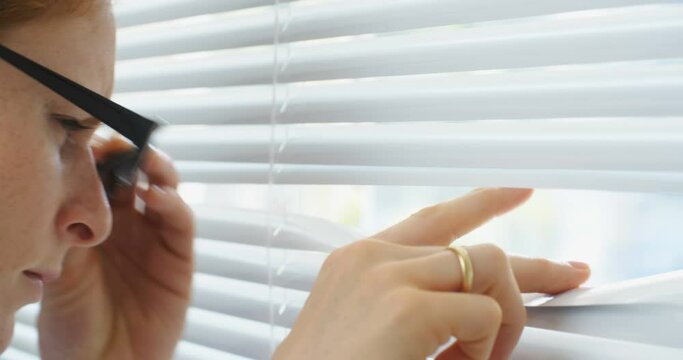 Curious business woman spying through window blinds, close up shot.