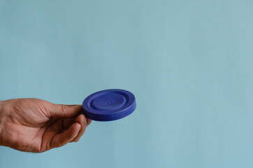 Hand holds a blue plastic lid for a can.