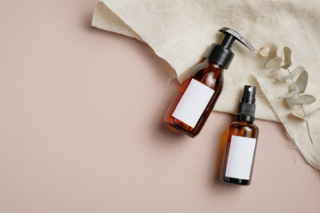 Amber glass cosmetic bottles set with towel and eucalyptus leaves on beige background. Beauty...