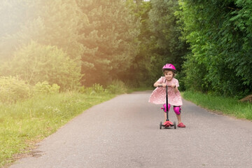 Portrait of active little toddler girl riding scooter on a village road outdoors