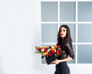 Beautiful young woman with a big bouquet of roses flowers in a black dress on a light background,