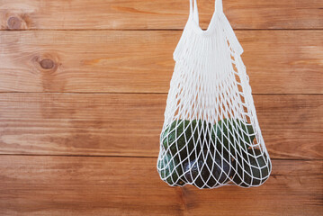 Reusable eco-friendly cotton mesh bag with avocado on wooden rustic background.