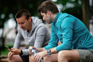 Fit young men taking rest from running. Two friends training outdoors.	