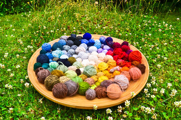 many colorful balls, clews, wads, ravels of wool, laying in a large wooden bowl standing on the...