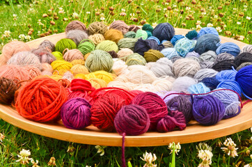 many colorful balls, clews, wads, ravels of wool, laying in a large wooden bowl standing on the...