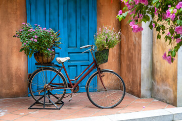 Obraz na płótnie Canvas Vintage bike with basket full of flowers next to an old building in Danang, Vietnam, close up