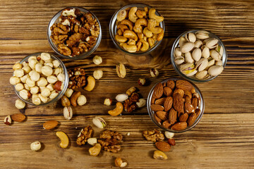 Assortment of nuts on wooden table. Almond, hazelnut, pistachio, walnut and cashew in glass bowls. Top view. Healthy eating concept
