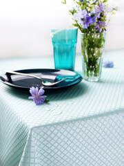 served table in blue, with cutlery, flowers and crockery. table setting details close up.