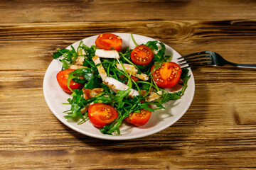 Tasty salad of fried chicken breast, fresh arugula and cherry tomatoes on wooden table