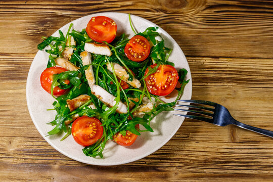 Tasty salad of fried chicken breast, fresh arugula and cherry tomatoes on wooden table. Top view