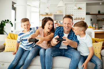 Husband and wife playing video games with joysticks in living room. Loving couple are playing video games with kids at home.	